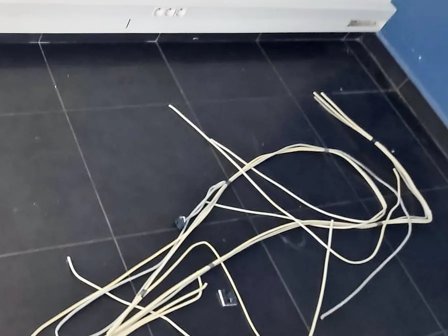 Câbles réseau beiges posés en tas sur un carrelage sombre, au pied d’une goulotte électrique