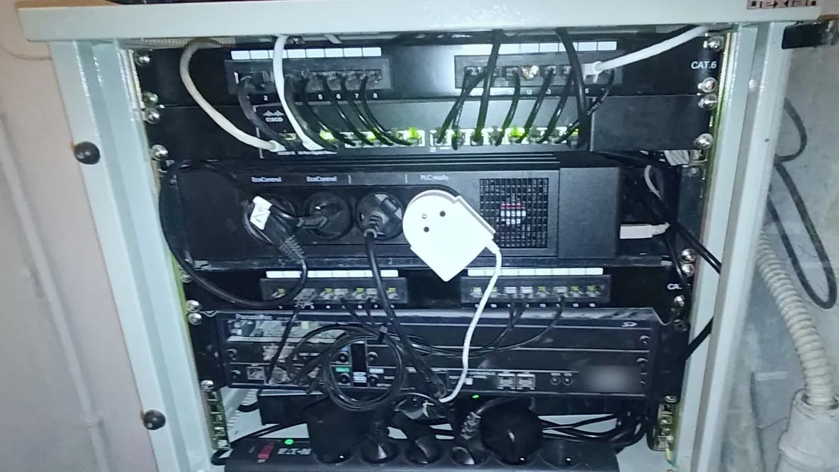 Baie réseau ouverte et rangée : panneaux de brassage, switch Cisco, câbles courts alignés, bloc de prises et standard téléphonique en dessous