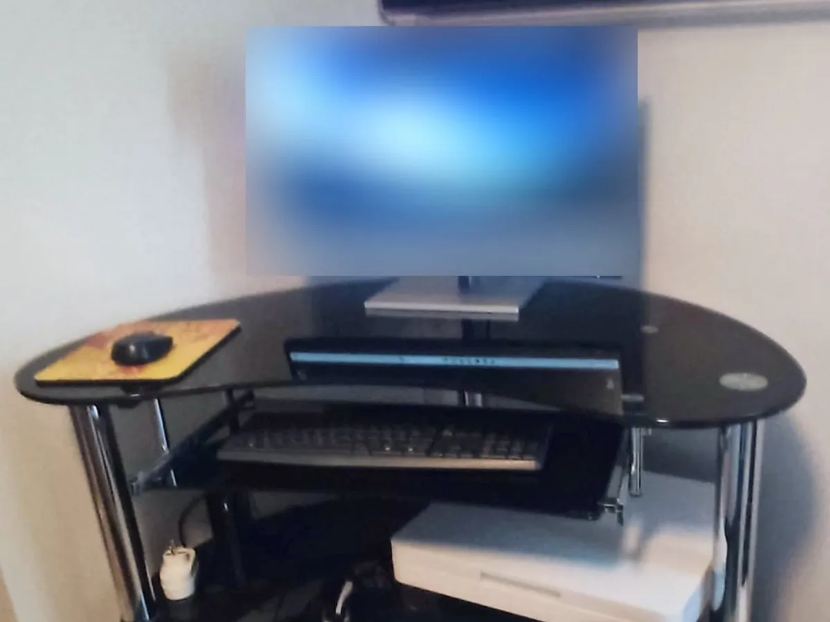 Nouvel écran, image floutée, posé sur un bureau d’angle en verre noir, clavier sur la tablette et imprimante multifonction Canon en dessous