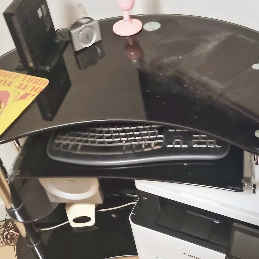 Bureau d’angle en verre noir avec clavier, tapis de souris et imprimante multifonction, avant l’installation du nouvel ordinateur