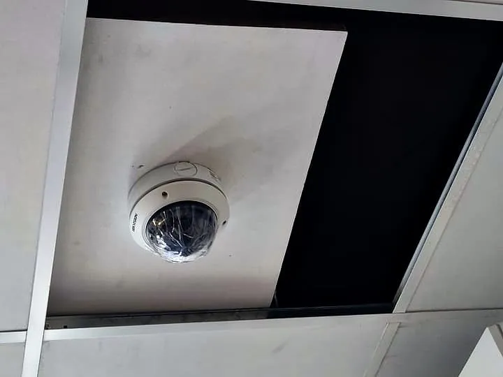 Caméra dôme de vidéosurveillance fixée sur une dalle de faux plafond, la dalle voisine ouverte