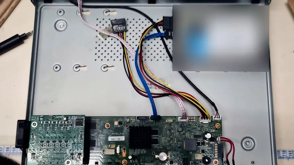 Enregistreur de vidéosurveillance ouvert sur une table, carte électronique et disque dur reliés par leurs câbles