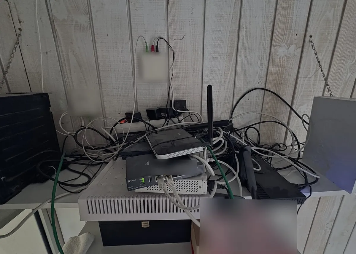 Étagère murale encombrée : routeurs, switch, box et câbles mêlés, sous les boîtiers fixés au mur