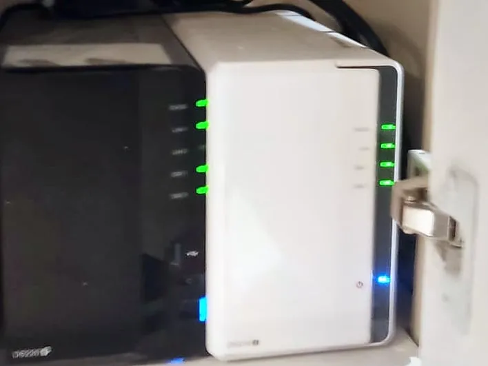 Deux NAS Synology, l’un noir et l’autre blanc, posés côte à côte sur l’étagère d’un placard, voyants allumés